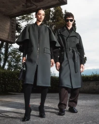 Two models wearing dark coats outdoors under a concrete structure for Ferrari FW24 campaign