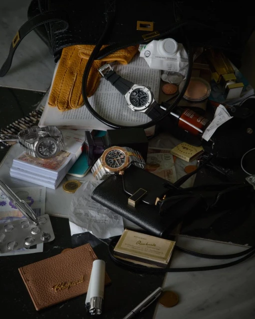 Still life of high-end luxury items, including watches, wallets, perfume, and other accessories, arranged on a black and white surface.