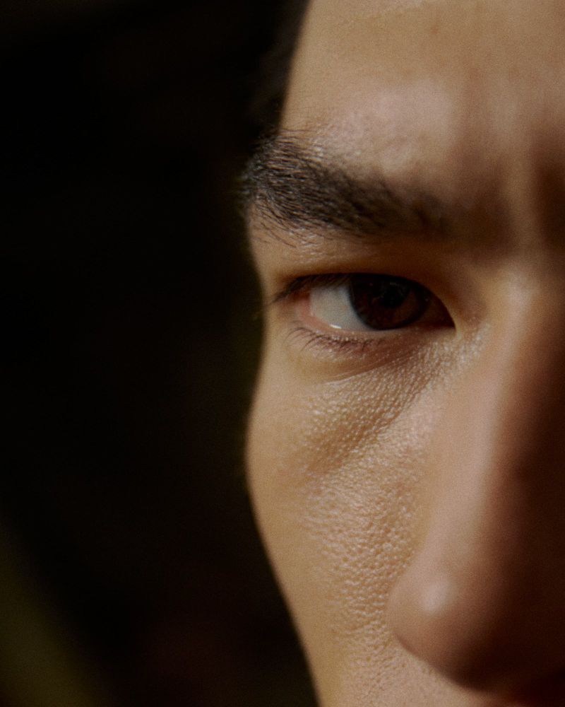Close-up of a face featuring brown eyes, eyebrow, and face details with soft light, set against a dark background.
