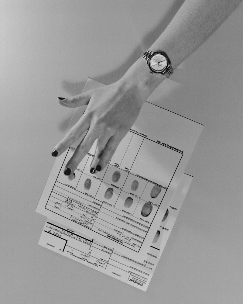 Close-up shot of a woman's hand wearing a watch, holding a fingerprint card in a brightly lit, neutral-toned indoor setting.