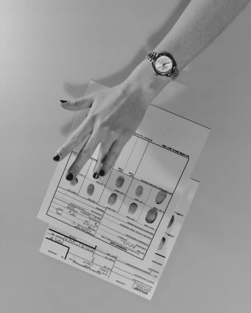 Close-up shot of a woman's hand wearing a watch, holding a fingerprint card in a brightly lit, neutral-toned indoor setting.
