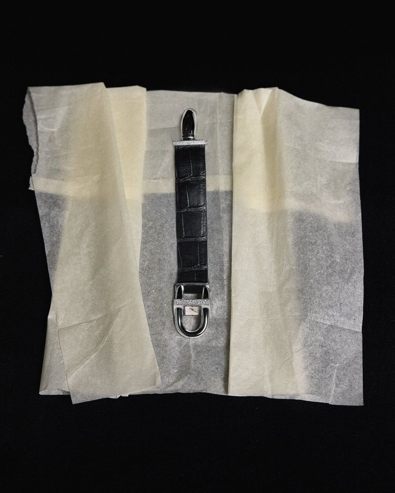 Close-up of a black leather crocodile-texture watch strap displayed on light tissue paper and set against a black background.