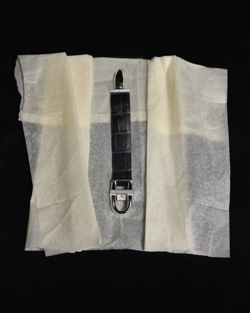 Close-up of a black leather crocodile-texture watch strap displayed on light tissue paper and set against a black background.