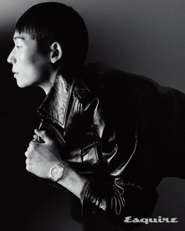 Monochrome portrait of a stylish adult man in a black leather jacket, posing with a watch on his wrist in a dark studio.