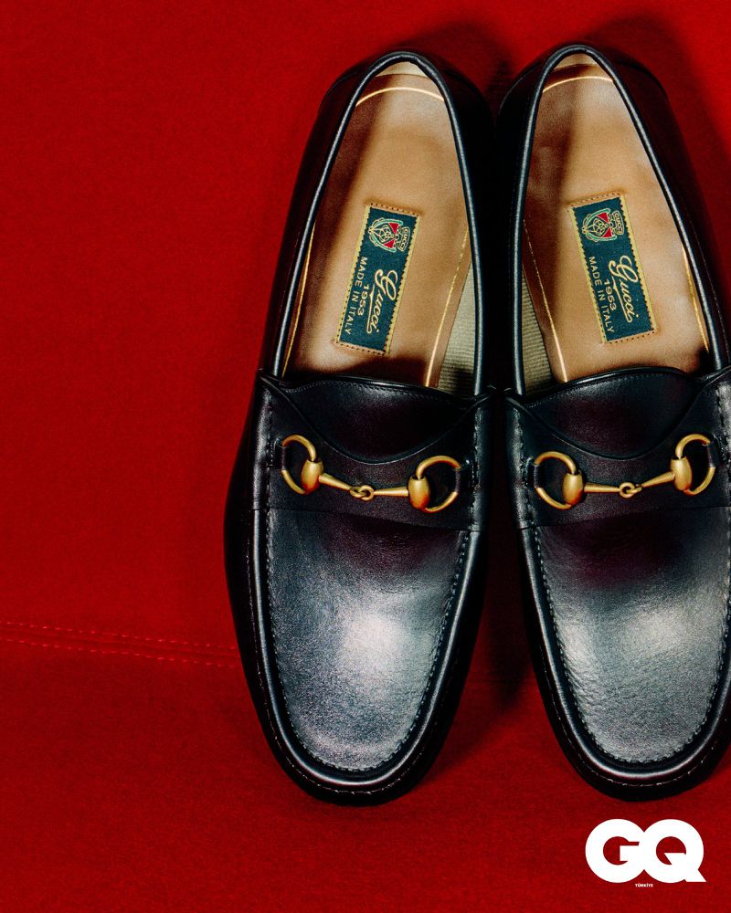 Close-up studio shot of a pair of black leather Gucci horsebit loafers with gold hardware, displayed on a red fabric background.