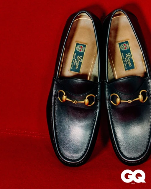 Close-up studio shot of a pair of black leather Gucci horsebit loafers with gold hardware, displayed on a red fabric background.