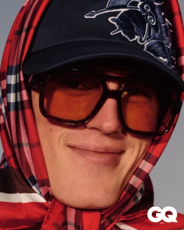 Portrait of a smiling adult male wearing a baseball cap, scarf, and sunglasses, close-up studio shot, fashion editorial.