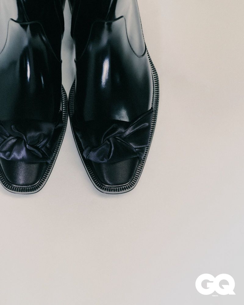 Close-up shot of a pair of shiny black leather dress shoes with satin knots on a light backdrop, exuding sophistication and style.
