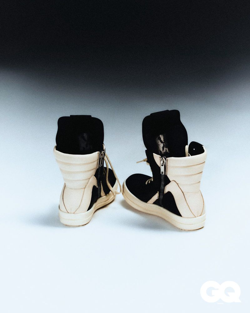 Close-up of a pair of black and beige high-top sneakers on a white surface against a dark gradient background, modern and fashionable footwear.