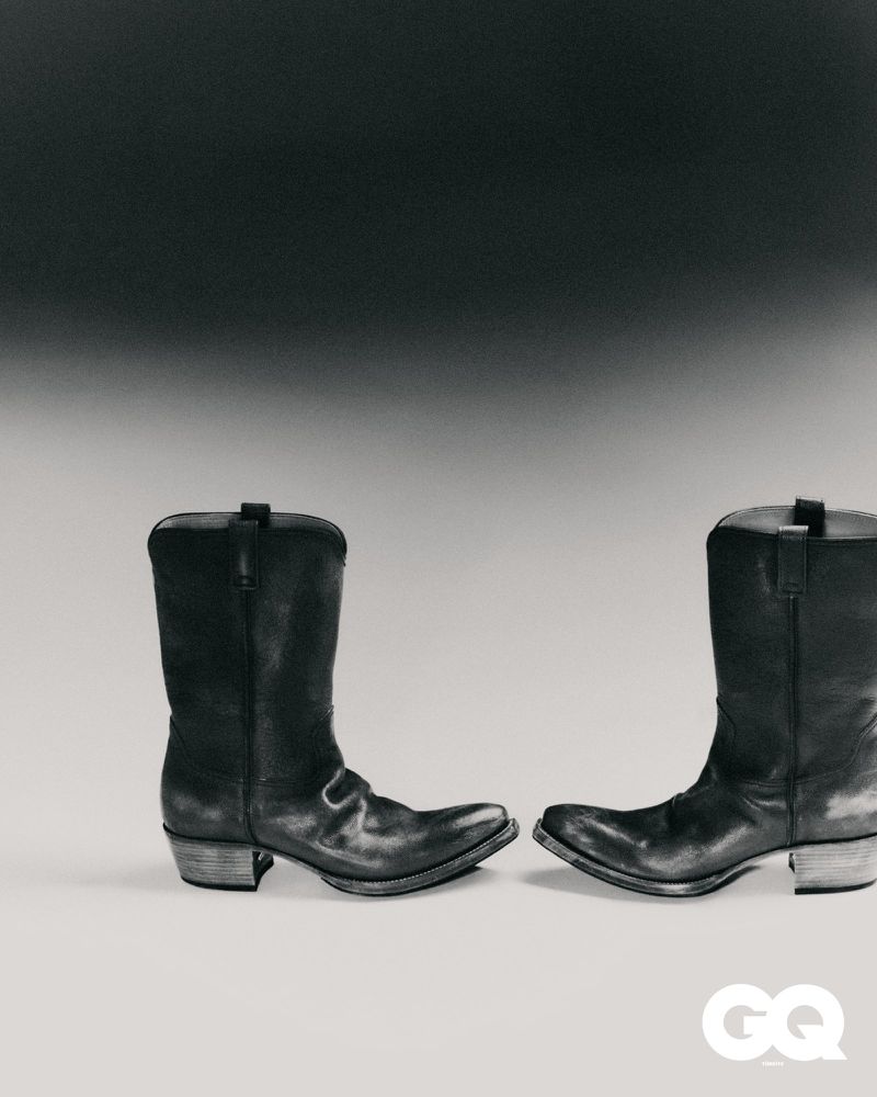 Studio shot featuring a pair of black leather cowboy boots on a gradient gray background, styled for a fashion editorial.