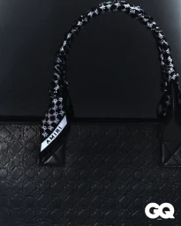 Close-up of a black embossed leather tote bag with a black and white patterned Amiri ribbon wrapped around the handle.