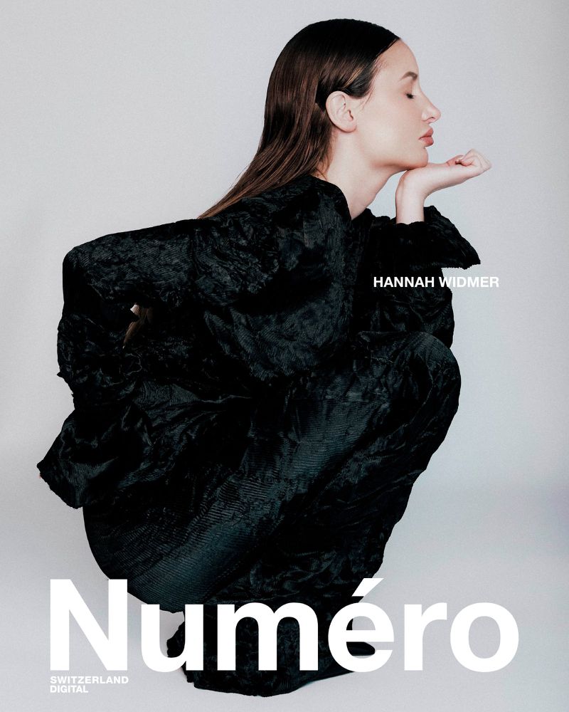 A woman with long brown hair poses in dark textured clothing against a soft gray backdrop with text overlay for a fashion magazine cover.