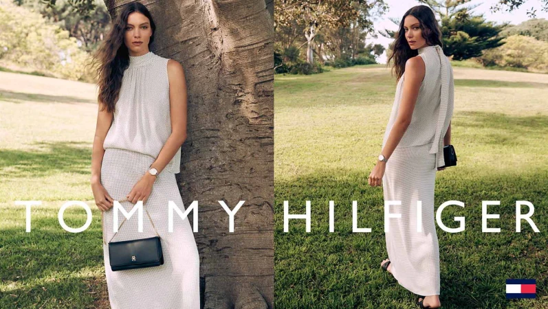 Model in a cream sleeveless top and matching maxi skirt standing by a large tree in a sunny park holding a black handbag