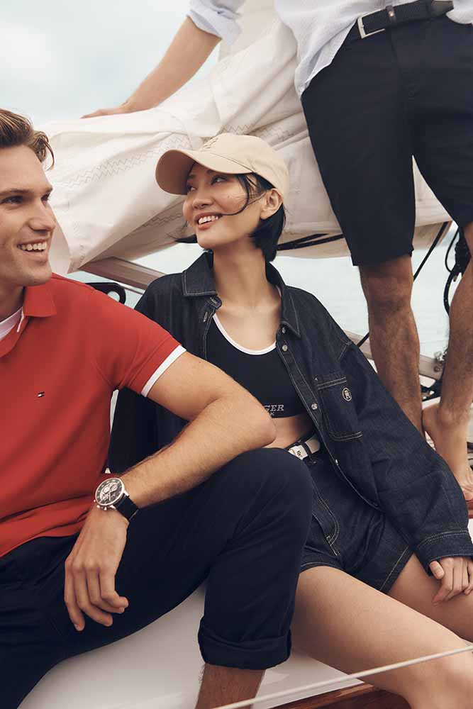 Group of three people wearing casual summer clothing on a boat, smiling and posing for fashion shot, featuring Tommy Hilfiger branded apparel.