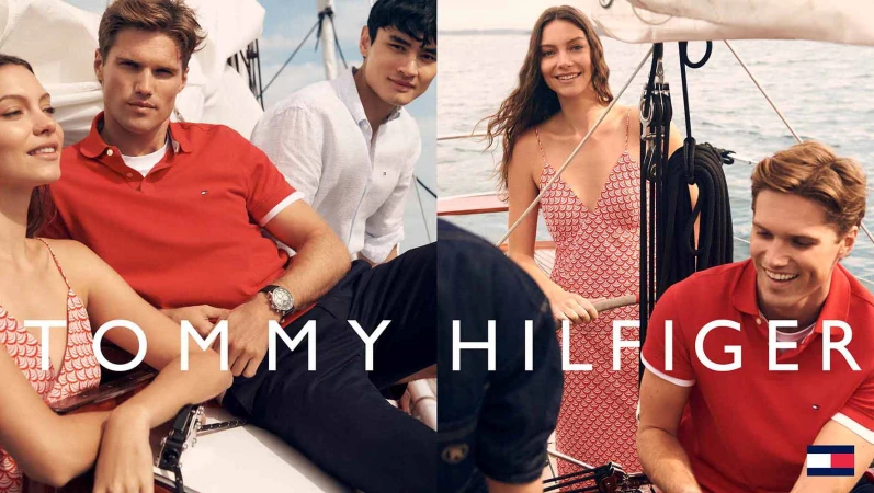 Group of casually dressed young adults in nautical themed Tommy Hilfiger fashion posing on a sailboat on a sunny day near the ocean.