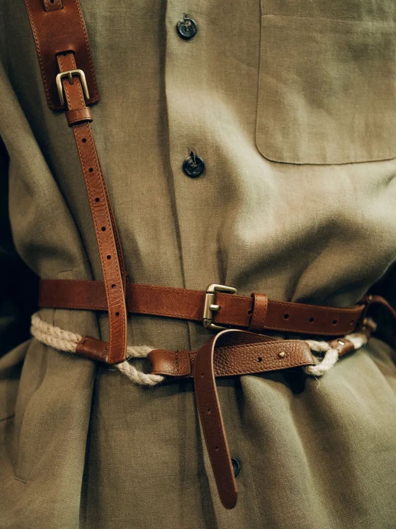 A detailed view of a linen shirt with brown leather belts and a rope belt cinched at the waist, showcasing fashion details.