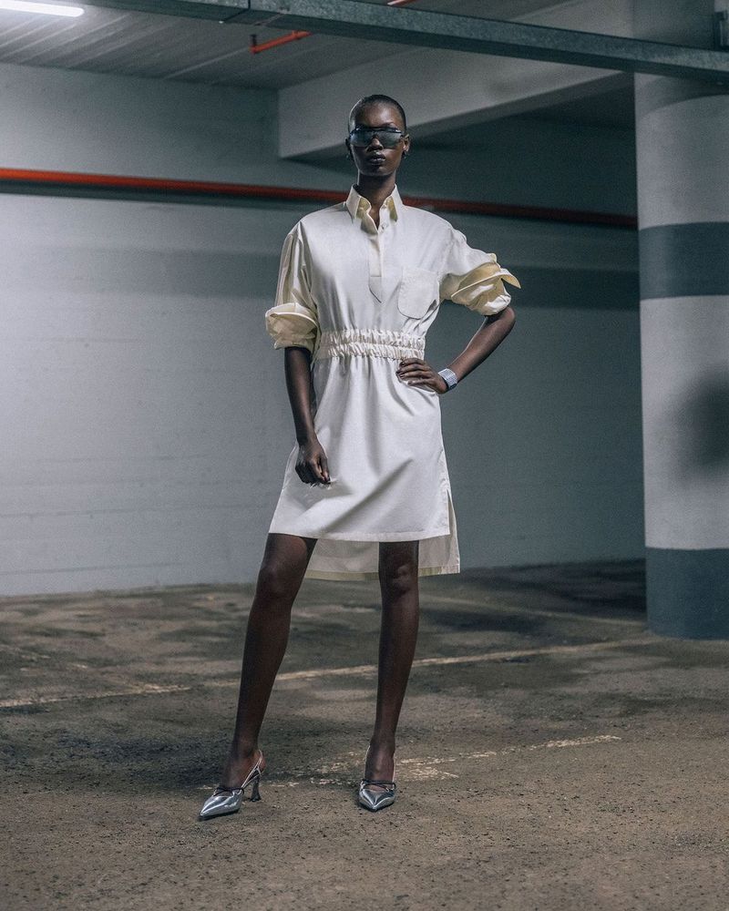 Model wearing a white dress and silver heels standing in a concrete parking garage for Ferrari campaign