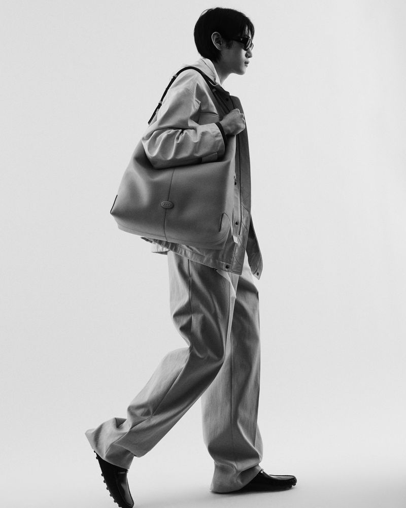 A person in casualwear walks in a photo studio setting, carrying a shoulder bag. Black and white fashion shot.