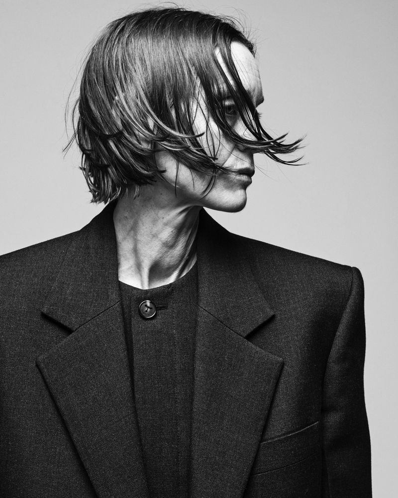 Monochrome portrait of a young adult male with dark hair styled forward, wearing a dark blazer in a studio setting against a neutral background.