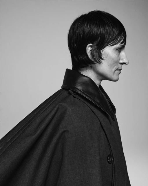 Portrait of a woman in a dark coat against a light backdrop, captured in a studio setting with soft lighting.