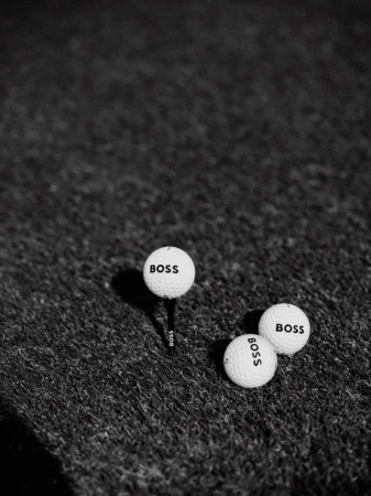 Black and white shot of three golf balls on a putting green, one ball is on a tee, all three golf balls have 'BOSS' printed on them.