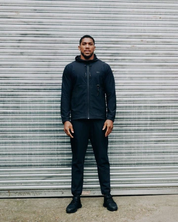 Full-length portrait of a man in dark athletic apparel standing against a corrugated metal background, creating a simple and focused composition.