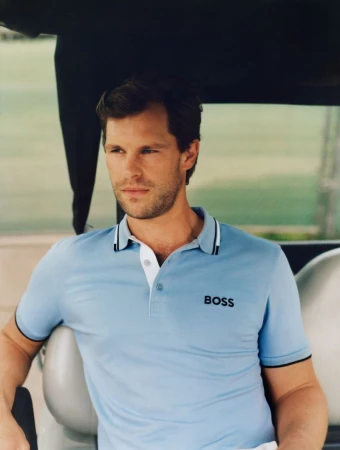 Adult male in a light blue polo shirt with a white collar and the word BOSS on it, sitting outdoors with blurred green background.
