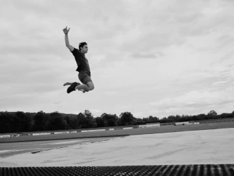 Monochrome action shot of tennis player Taylor Fritz mid-air jumping over an athletic field
