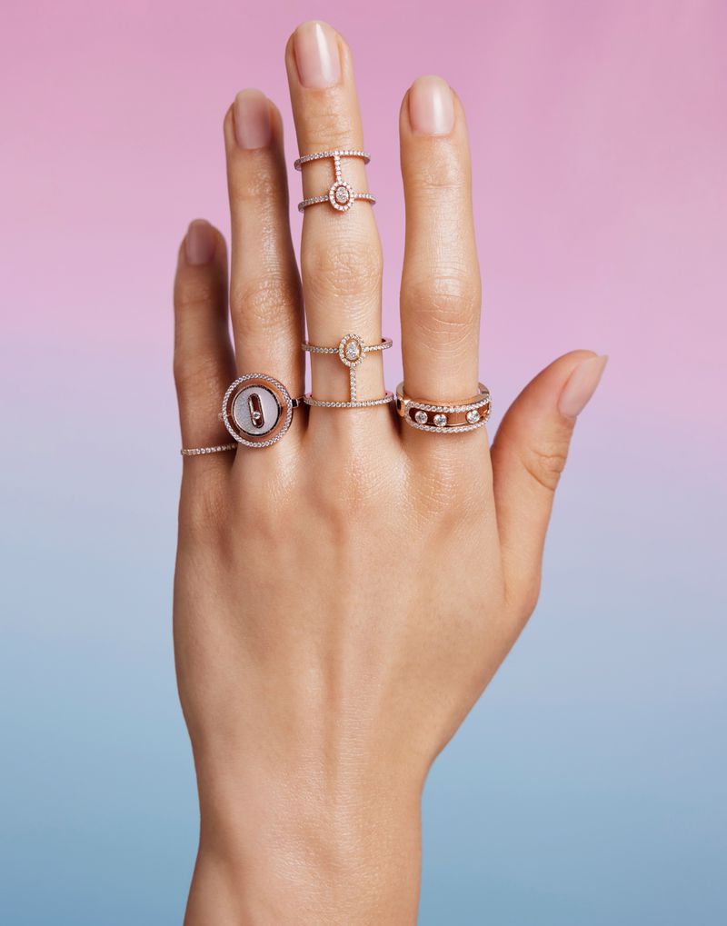 Close-up of a hand displaying several diamond rings against a pink and blue gradient background for Messika