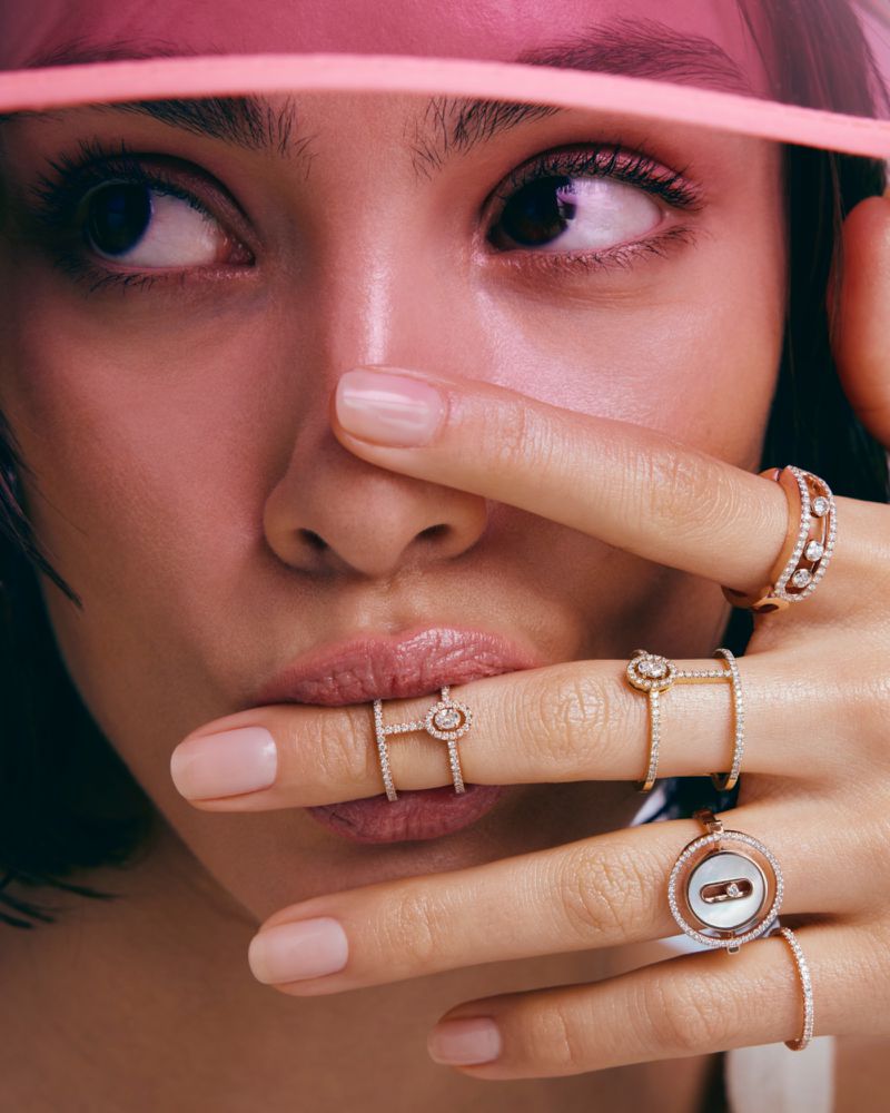 Close-up studio shot of a woman wearing several diamond rings on her fingers, and a pink transparent visor on her head.