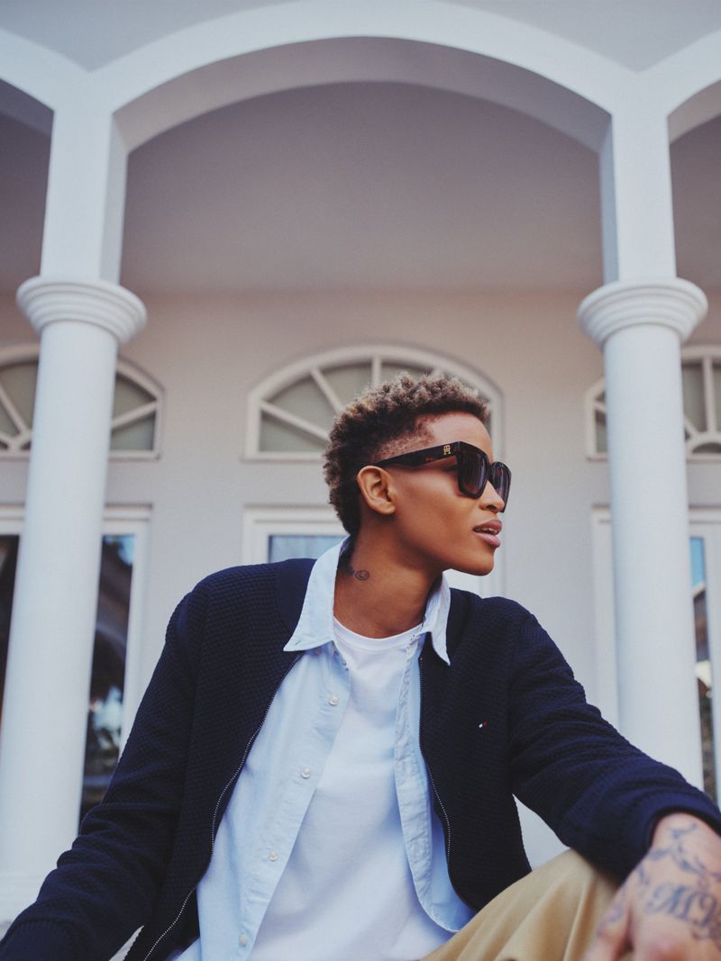 Stylish woman in sunglasses poses confidently in front of a white building with classic architectural details and neutral tones.