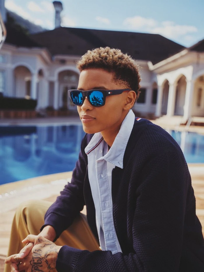 Model wearing dark blue sunglasses and a navy cardigan by a swimming pool for Tommy Hilfiger Eyewear