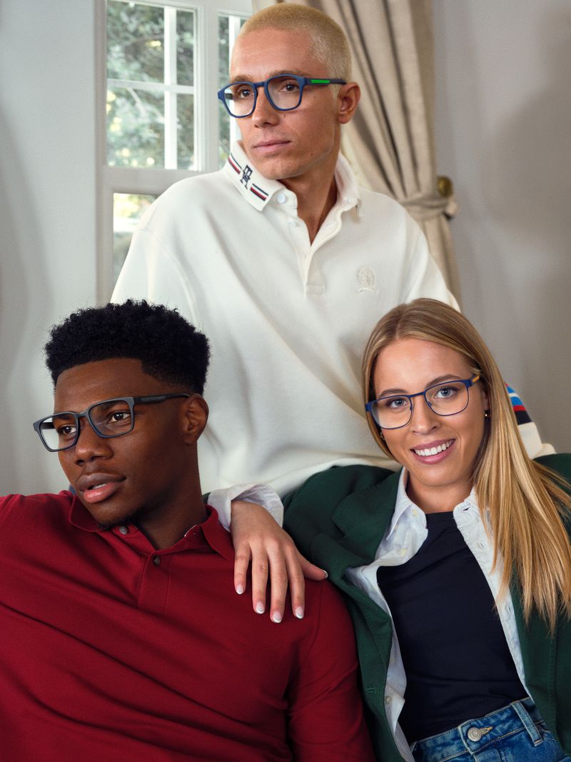 Three people pose indoors: a blonde man wearing glasses standing with one black man in red and blonde woman in blue jeans.