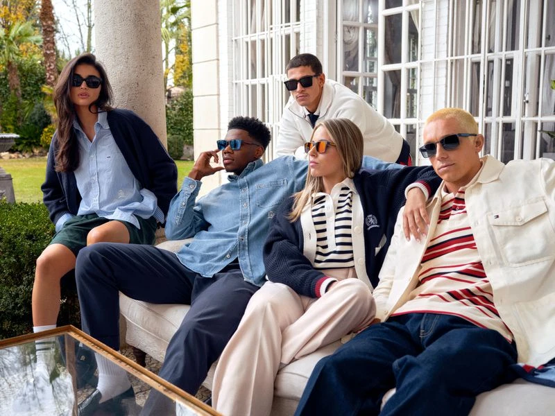 Group of five people wearing sunglasses and casual clothing, posing outdoors with white pillars and green foliage backdrop.