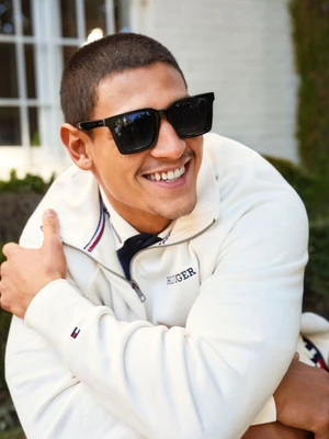 Smiling man wearing black sunglasses and a white zip-up sweatshirt outdoors