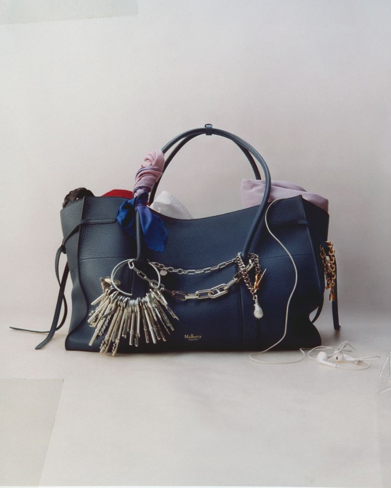Navy blue leather Mulberry handbag with scarves, jewelry, and earbud headphones, creating a detailed fashion product still life shot.