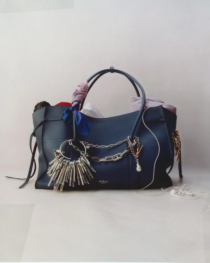 Dark blue leather tote bag accessorized with chains, keys, and colorful ribbons against a neutral background.