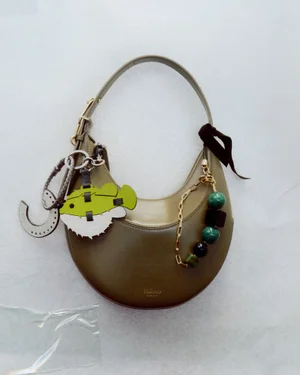 Olive green leather shoulder bag decorated with charms against a plain white background for Mulberry Charms.