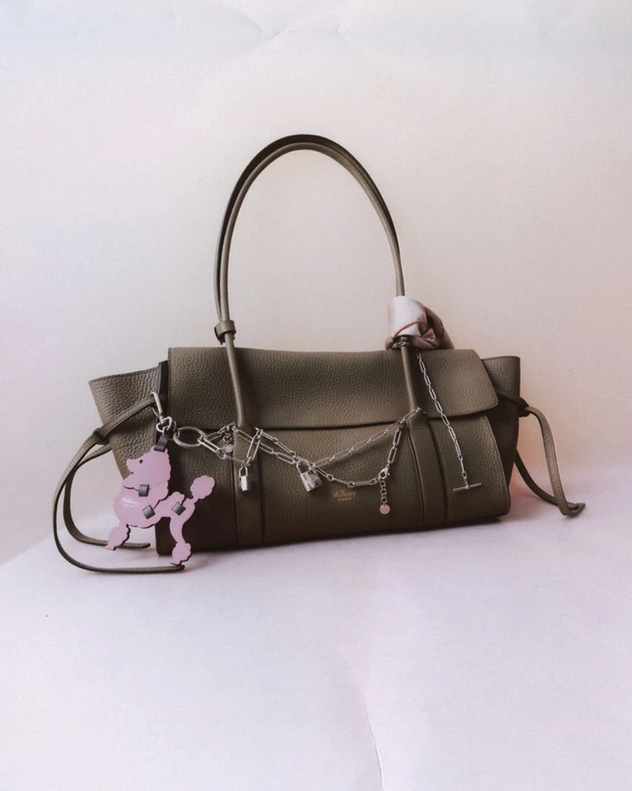 Olive green leather handbag with silver chain charms and a pink poodle keyring against a white backdrop for Mulberry Charms.