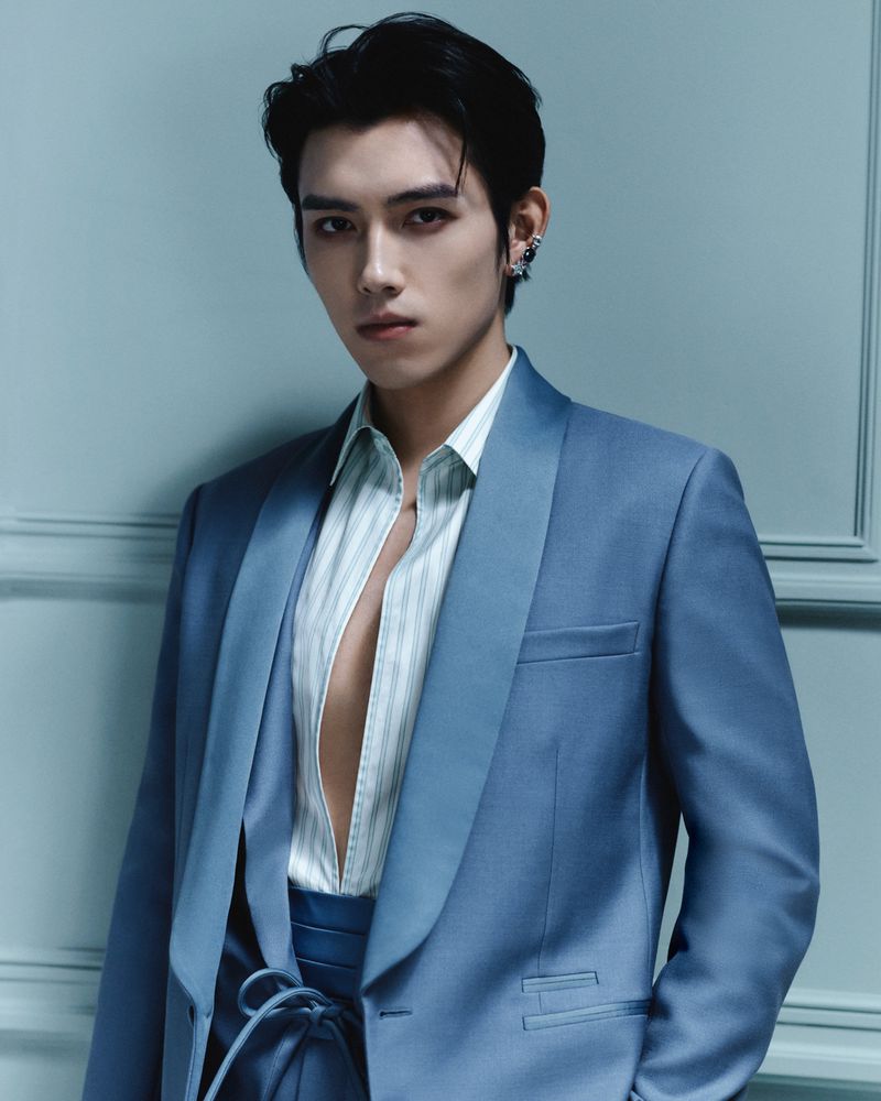 Portrait of a handsome adult male with dark hair, wearing a light blue suit and striped shirt, gazing intensely at the camera.