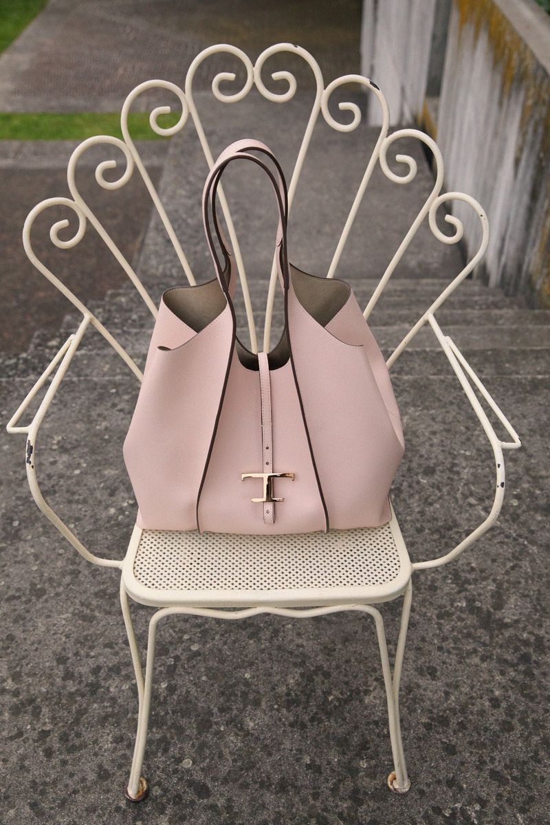 Blush-pink leather Tod's tote bag on a decorative white metal chair, sitting on stone steps, offering a luxury fashion product shot.