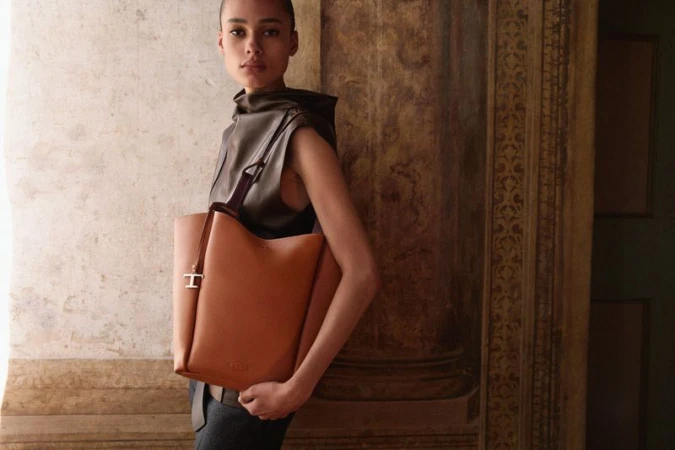 Model standing in classic interior holding a large brown leather shoulder bag for Tod's campaign.