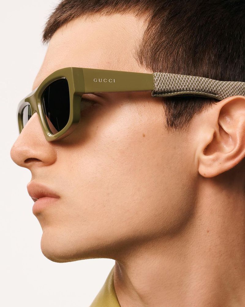 Close-up of a man wearing olive green Gucci sunglasses with a gray strap, showcasing fashion eyewear and male style.