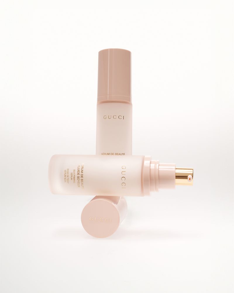 Gucci beauty serum bottles in soft pink tones, stacked creatively on a white background, showcasing elegant skincare presentation.