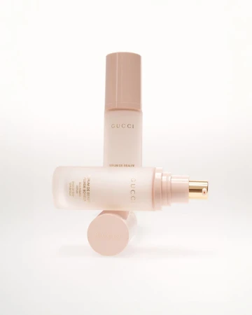 Gucci beauty serum bottles in soft pink tones, stacked creatively on a white background, showcasing elegant skincare presentation.