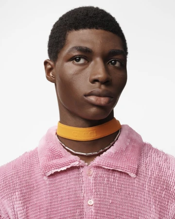 Close-up portrait of a Black male model wearing an orange Gucci choker and a textured pink collared shirt against a white background.