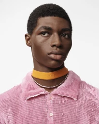 Close-up portrait of a Black male model wearing an orange Gucci choker and a textured pink collared shirt against a white background.