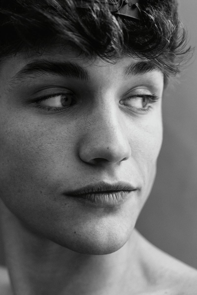 Black and white portrait of a young adult male looking off to the side with a neutral facial expression and tousled dark hair.