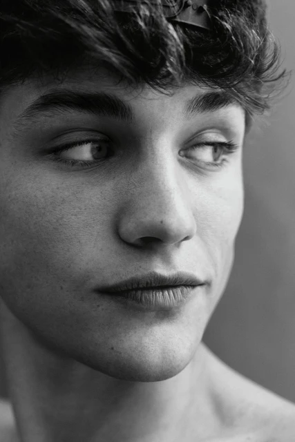 Black and white portrait of a young adult male looking off to the side with a neutral facial expression and tousled dark hair.