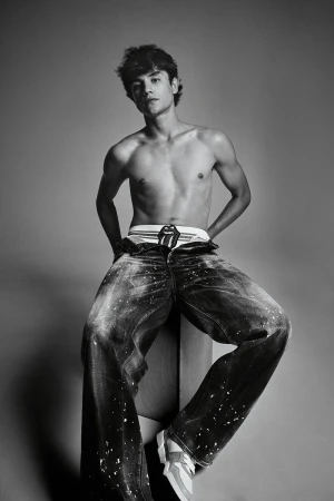 Monochrome studio portrait of a young man seated wearing distressed denim jeans and branded underwear